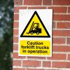CA-FORK-PORT-001-07-BRICK-WALL-WM-1.jpg Caution Forklift Trucks in Operation Sign - Active MHE Warning | A5, A4, A3 | Easi-Signs